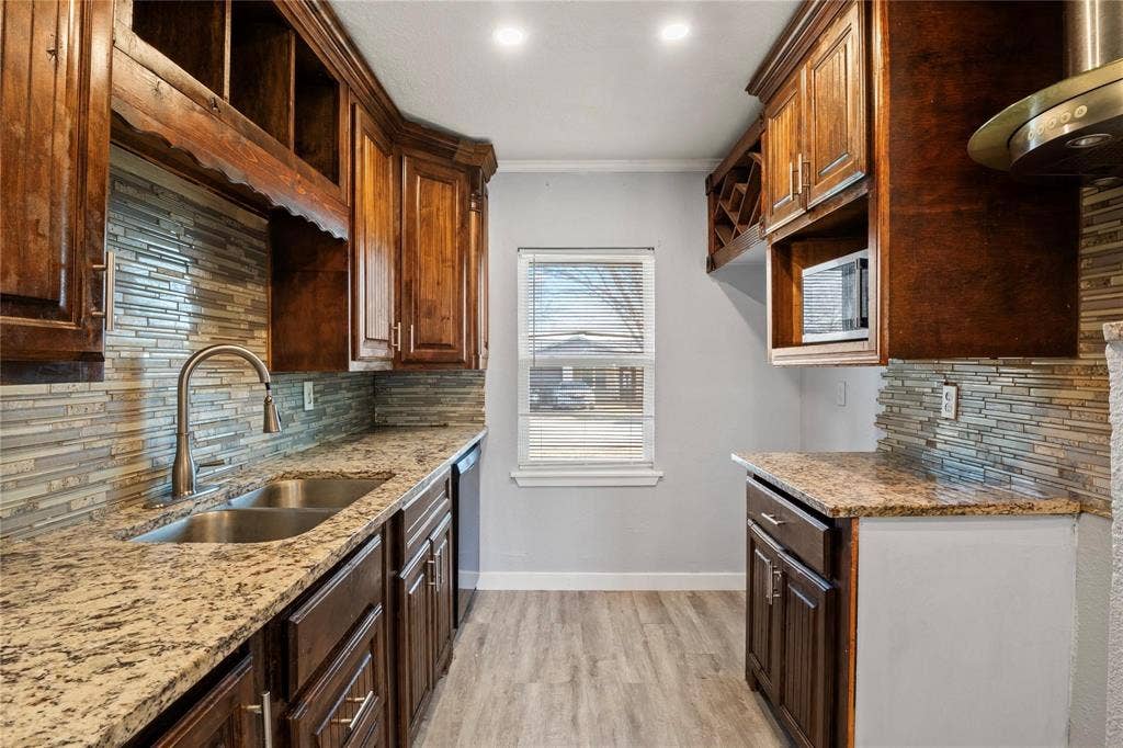 6543 Gentle River, Dallas, TX 75241 Kitchen featuring stained wood cabinetry, stone-patterned countertops, a stacked stone backsplash, wood-finish flooring, and a stainless steel gooseneck faucet