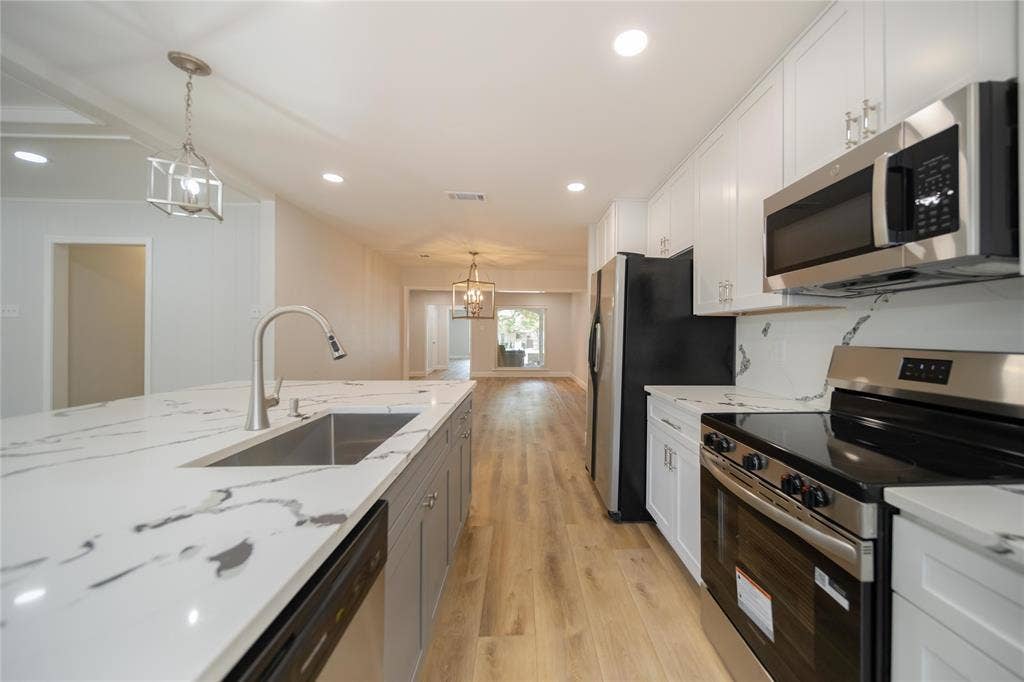 4333 Harvest Hill Road, Dallas, TX 75244 Kitchen featuring an expansive island with a waterfall edge, quartz countertops, white shaker-style cabinetry, stainless steel appliances, and wood-finish flooring
