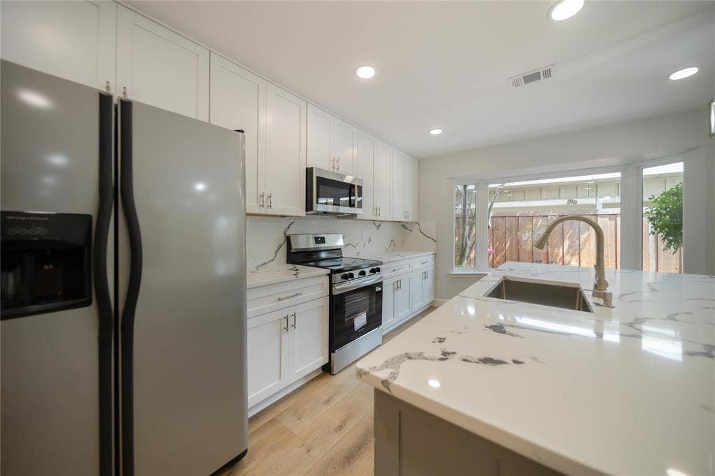 4333 Harvest Hill Road, Dallas, TX 75244 Kitchen featuring white Shaker-style cabinetry, quartz countertops with veining, wood-finish flooring, stainless steel appliances, and a central island with an undermount sink