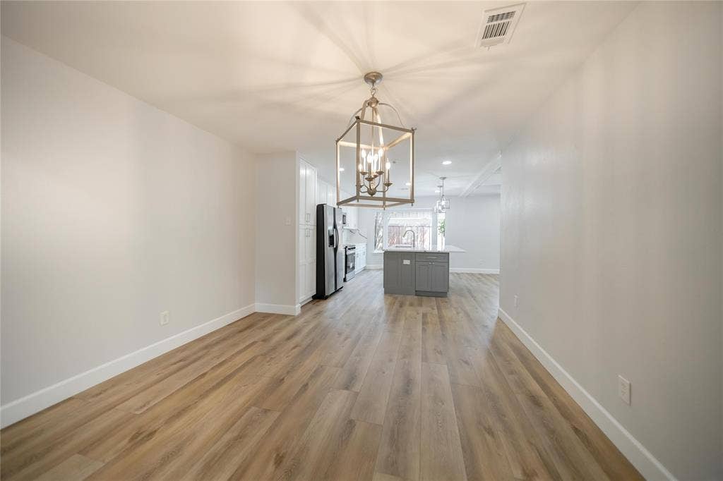 4333 Harvest Hill Road, Dallas, TX 75244 Open-concept area featuring wood-finish flooring, a geometric metal-frame chandelier, and a central kitchen island with cabinetry