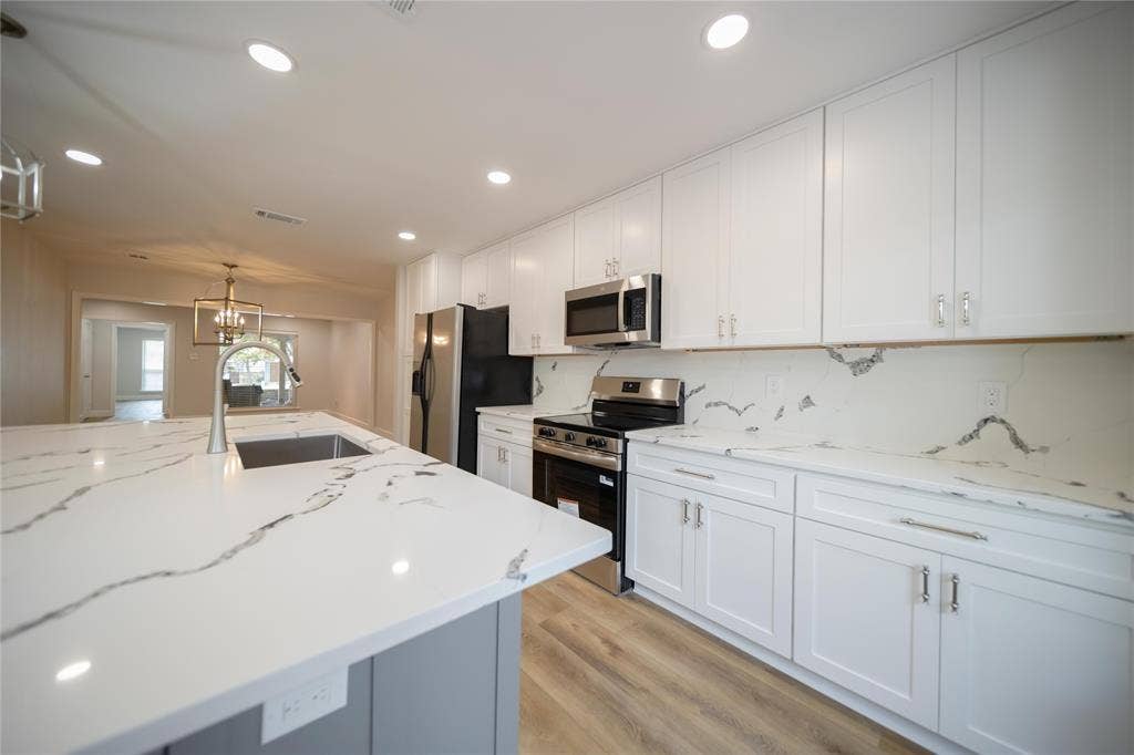 4333 Harvest Hill Road, Dallas, TX 75244 Kitchen featuring white shaker cabinetry, stone-patterned countertops, a coordinating full-height backsplash, stainless steel appliances, and a central island with a built-in sink
