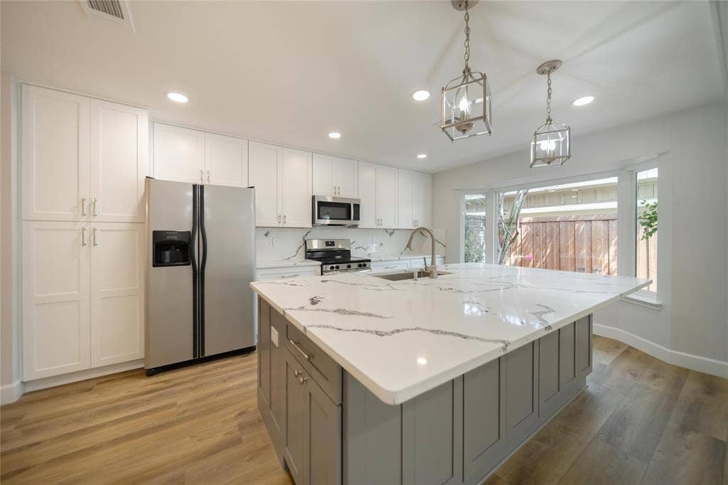 4333 Harvest Hill Road, Dallas, TX 75244 Kitchen featuring white cabinetry, an expansive center island with stone-finish countertops, stainless steel appliances, wood-finish flooring, and dual lantern-style pendant lights