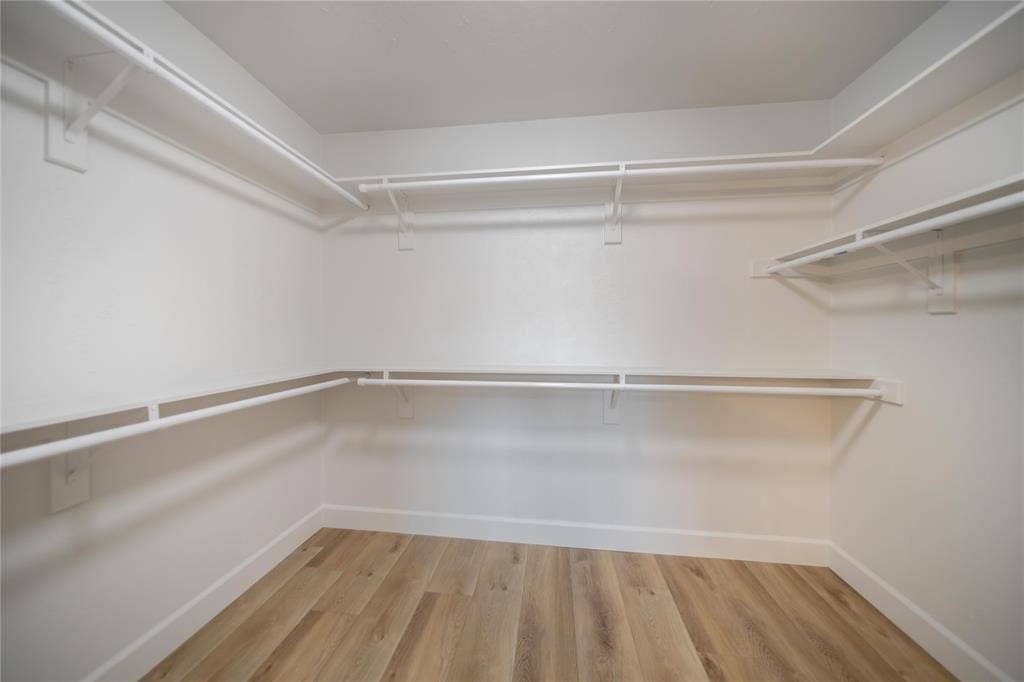 4333 Harvest Hill Road, Dallas, TX 75244 Walk-in storage space featuring wood-finish flooring, white walls, and tiered wall-mounted shelving with integrated hanging rods