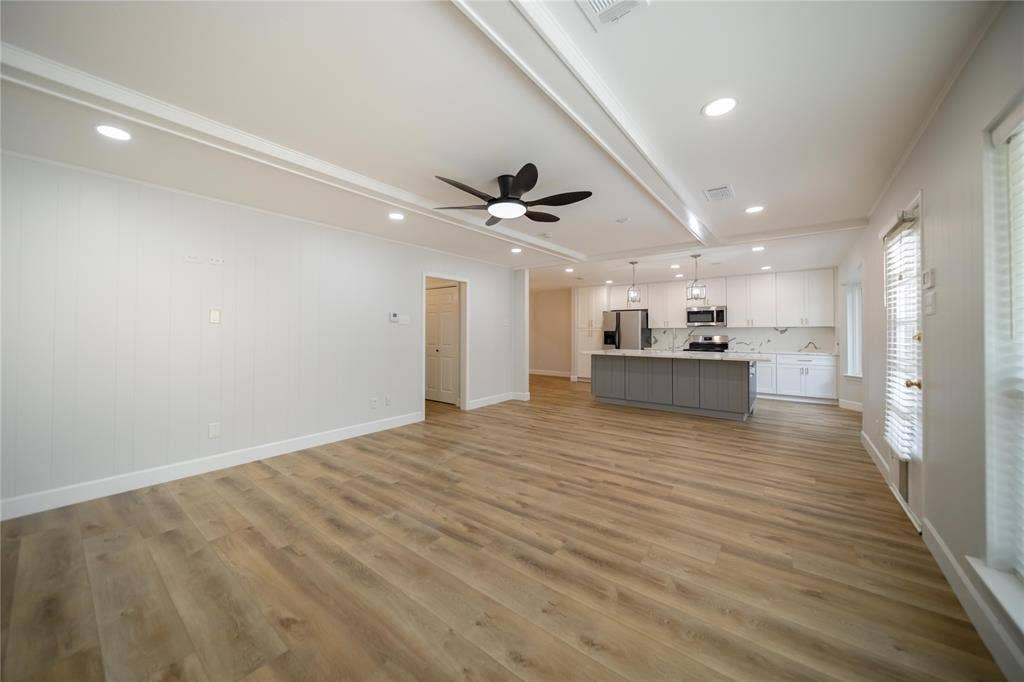 4333 Harvest Hill Road, Dallas, TX 75244 Open-concept interior featuring wood-finish flooring, tray ceiling with recessed lighting, kitchen island with stone-finish countertop, white shaker-style cabinetry, and matte black ceiling fan