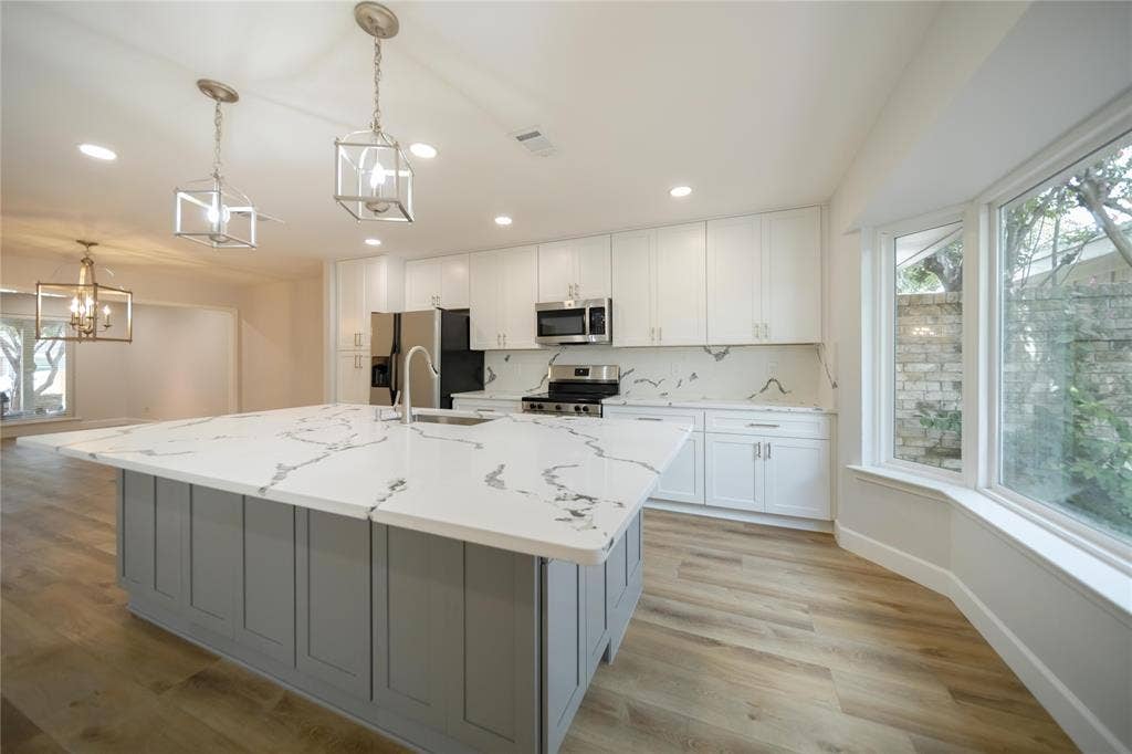 4333 Harvest Hill Road, Dallas, TX 75244 Kitchen featuring an oversized central island with stone-finish countertops, white cabinetry, stainless steel appliances, pendant lighting, and wood-finish flooring