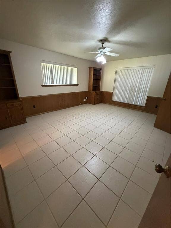 305 Westway Circle, Rockwall, TX 75087 Room featuring ceramic tile flooring, wood paneling, dual built-in wooden shelving units, and a ceiling fan with integrated light fixture