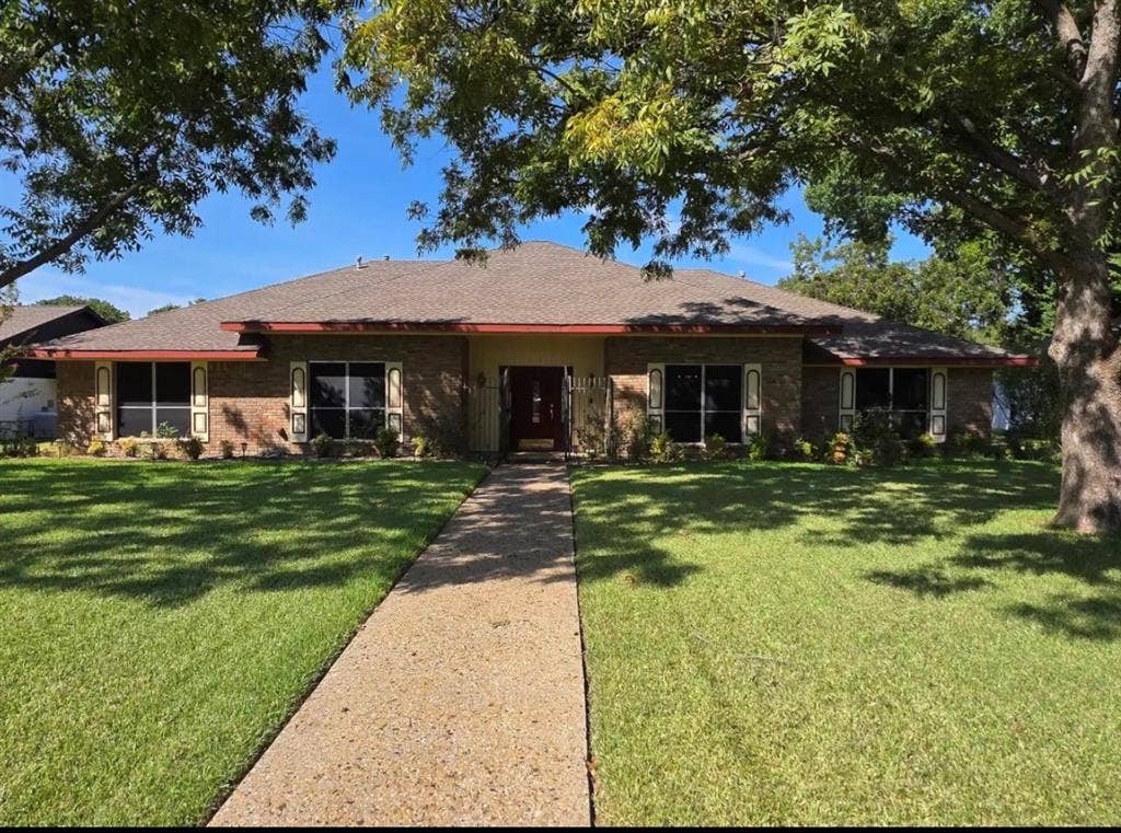 305 Westway Circle, Rockwall, TX 75087 Single-story brick exterior featuring a hip roof, central entryway with detailed front door, rectangular window shutters, and a concrete walkway