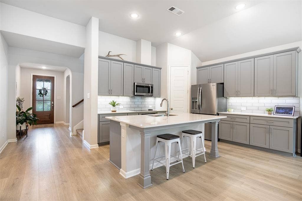Beautiful kitchen features grey cabinetry, generous island with seating area, subway tile backsplash, and pantry.