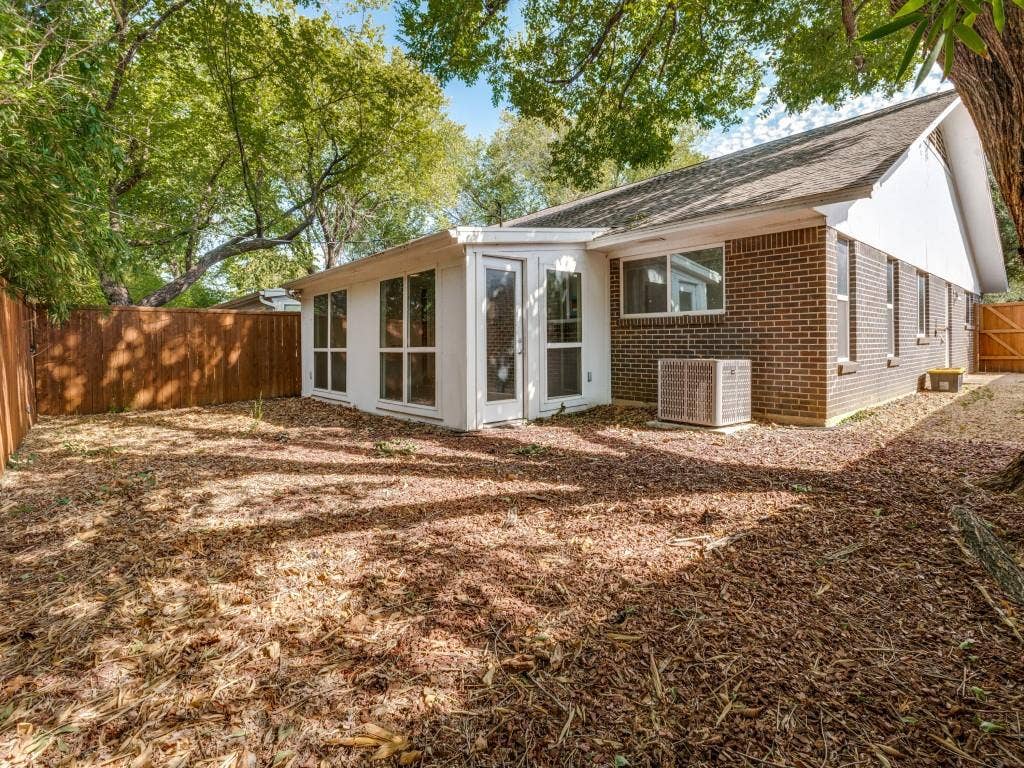 11321 Park Central Place, Dallas, TX 75230 Brick exterior, enclosed sunroom with glass paneled doors, large-format windows, wood privacy fencing, and mature trees