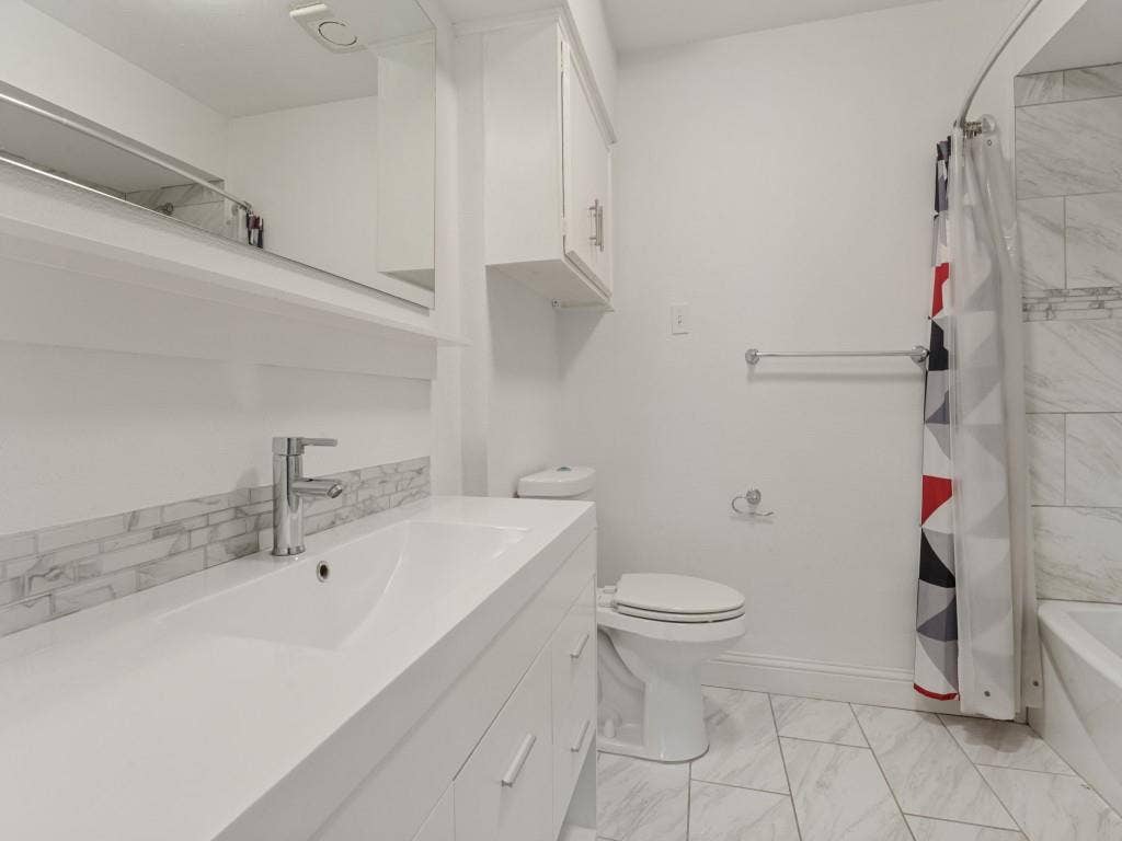 11321 Park Central Place, Dallas, TX 75230 Bathroom featuring a white vanity with an integrated sink, polished chrome faucet, stone-tile backsplash, and tile flooring arranged in a herringbone pattern