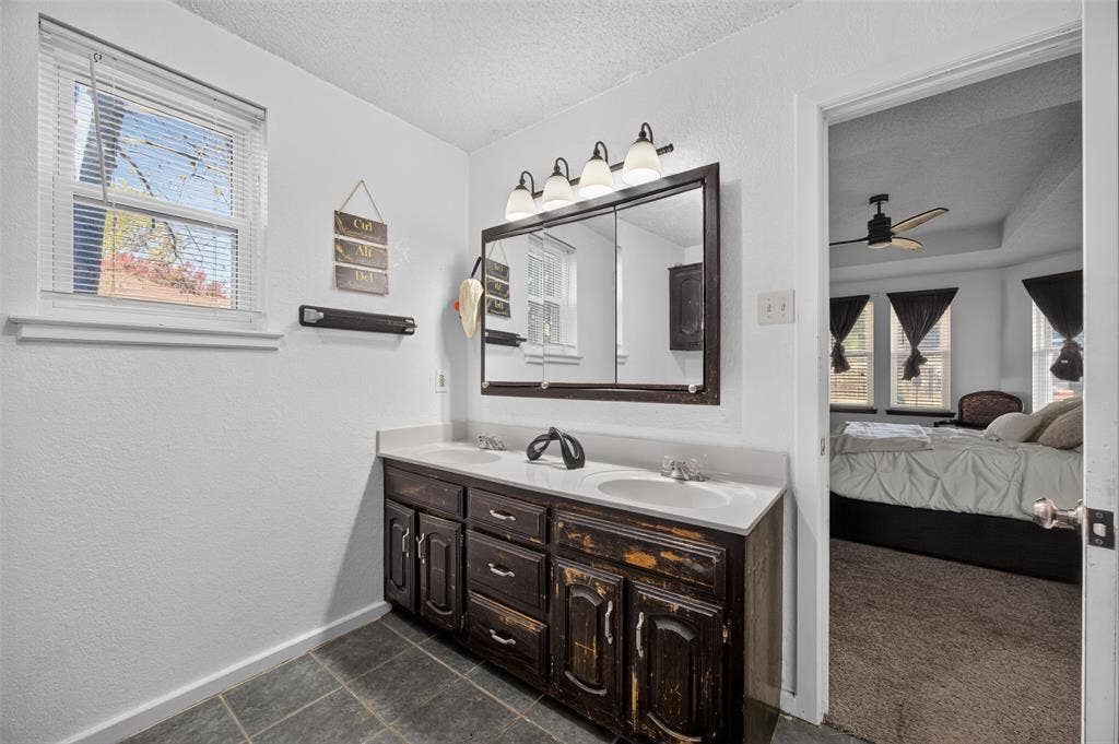 113 Dove Avenue, Red Oak, TX 75154 Dual-sink vanity with dark wood cabinetry and a solid-surface countertop, illuminated by a four-light fixture above a tri-fold medicine cabinet, complemented by large-format tile flooring