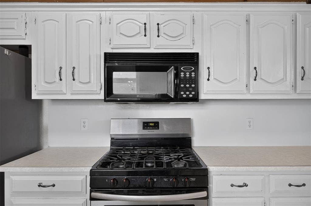 113 Dove Avenue, Red Oak, TX 75154 White cabinetry with traditional panel detailing, built-in over-the-range microwave, stainless steel gas range, and expansive solid-surface countertops