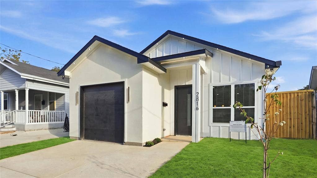 2816 Marburg Street, Dallas, TX 75215 Modern exterior featuring board-and-batten siding, a single-car garage with black door, concrete driveway, recessed soffit lighting, and high-contrast dark window trim