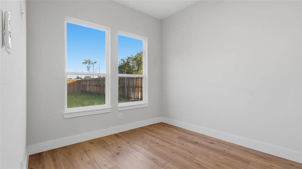 2816 Marburg Street, Dallas, TX 75215 Neutral-toned interior space featuring light wood-finish flooring, dual-pane windows with white trim, and a fenced exterior area