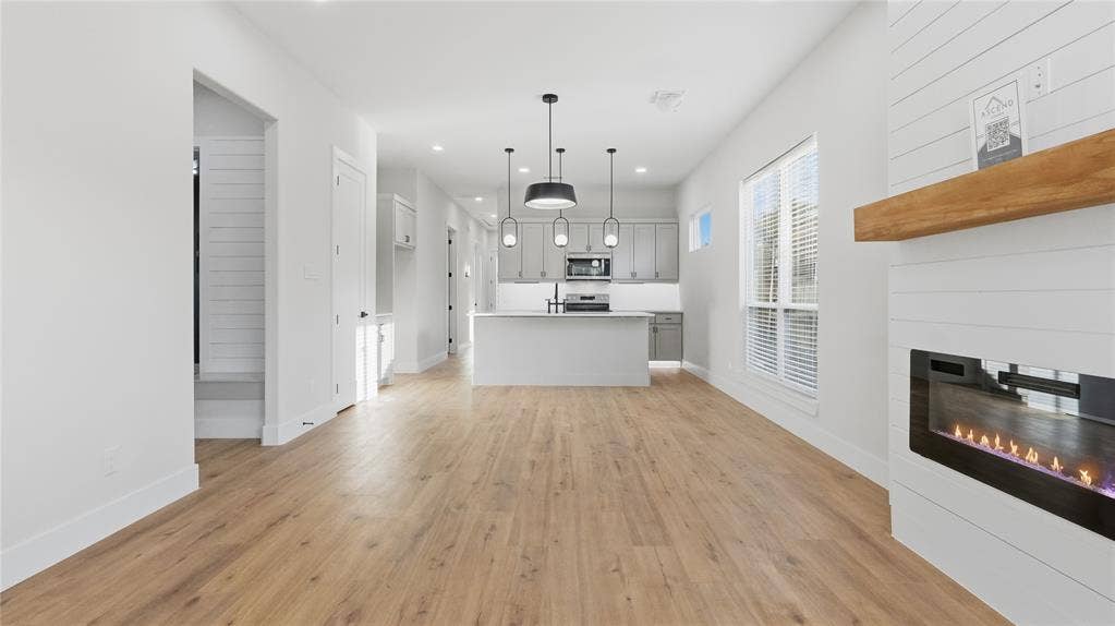 2816 Marburg Street, Dallas, TX 75215 Open floor plan featuring wood-finish flooring, built-in horizontal plank fireplace surround with a natural wood mantel, recessed lighting, and kitchen island with pendant lighting