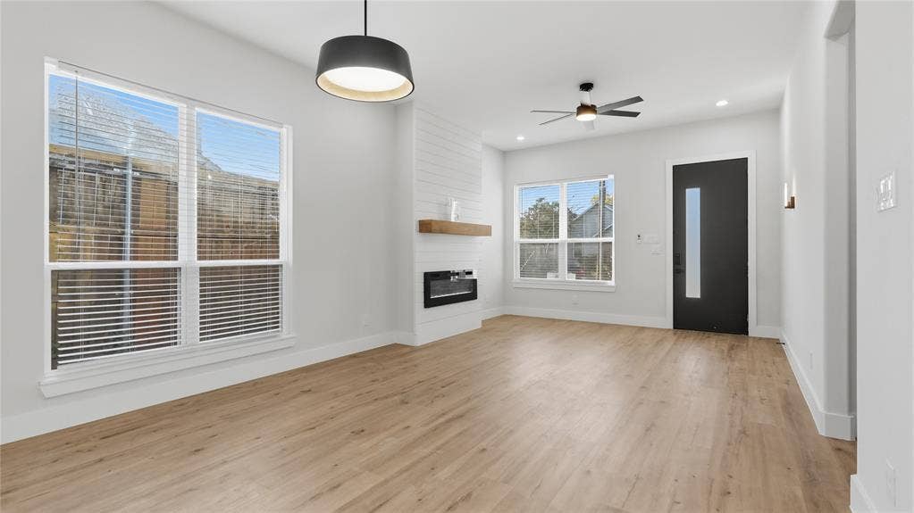 2816 Marburg Street, Dallas, TX 75215 Living area featuring wood-finish flooring, a linear fireplace with a shiplap surround and wood mantel, a contemporary drum pendant light, and a modern entry door with a vertical glass inset