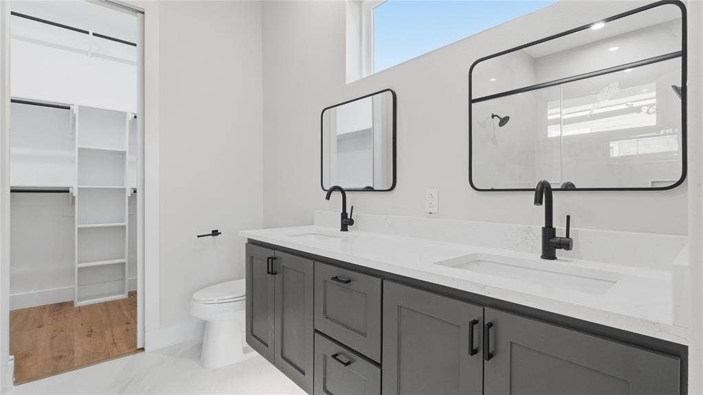 2816 Marburg Street, Dallas, TX 75215 Double vanity featuring dark cabinetry, white countertops with integrated sinks, matte black fixtures, and rectangular mirrors, complemented by a walk-in closet with built-in shelving