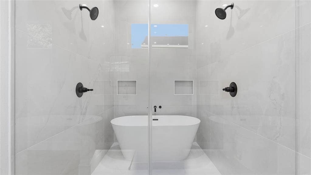 2816 Marburg Street, Dallas, TX 75215 Wet room featuring a freestanding soaking tub, dual wall-mounted showerheads, matte black fixtures, full-height tile surround, and recessed wall niches