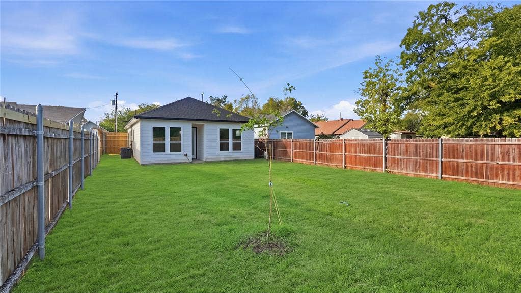 2816 Marburg Street, Dallas, TX 75215 Expansive backyard featuring a large grass lawn, perimeter wood fencing, and a light-toned siding exterior with a dark-finish roof