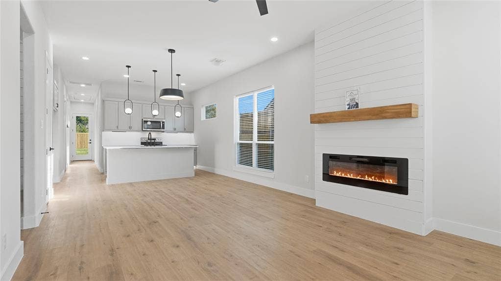2816 Marburg Street, Dallas, TX 75215 Open-concept area featuring wood-finish flooring, a white shiplap fireplace surround with a natural wood mantel, an electric wall-mounted fireplace, a kitchen island with pendant lighting, and recessed ceiling lighting