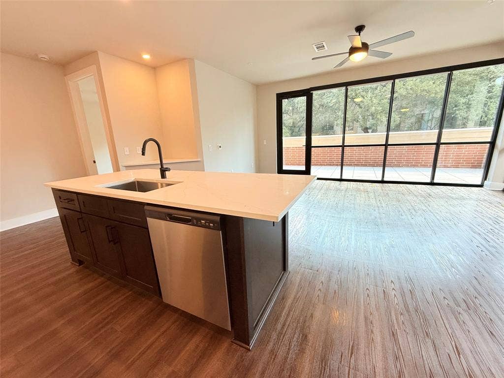 3255 Carlisle Street, #1207, Dallas, TX 75204 Kitchen featuring stainless steel dishwasher, open floor plan, dark wood-style flooring, dark brown cabinetry, and a kitchen island with sink