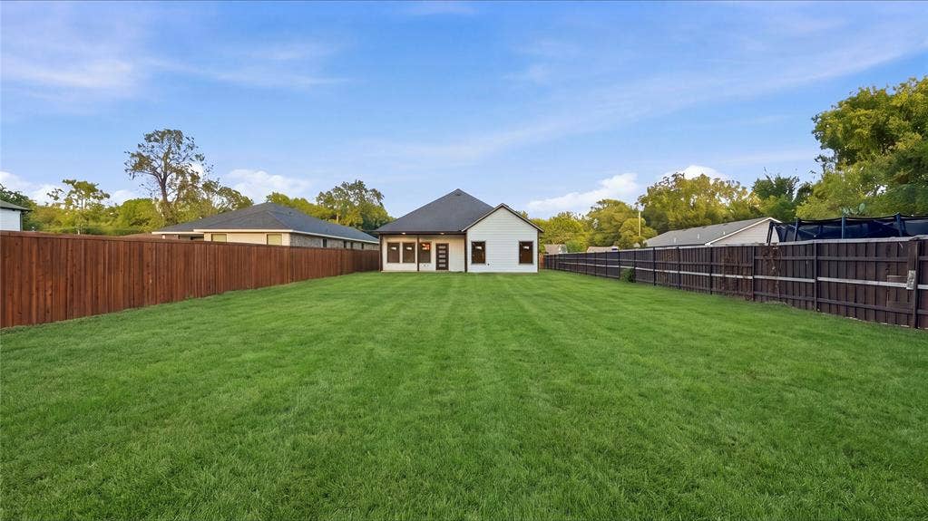 Expansive backyard featuring a large grass lawn, perimeter wood privacy fencing, and a covered rear patio
