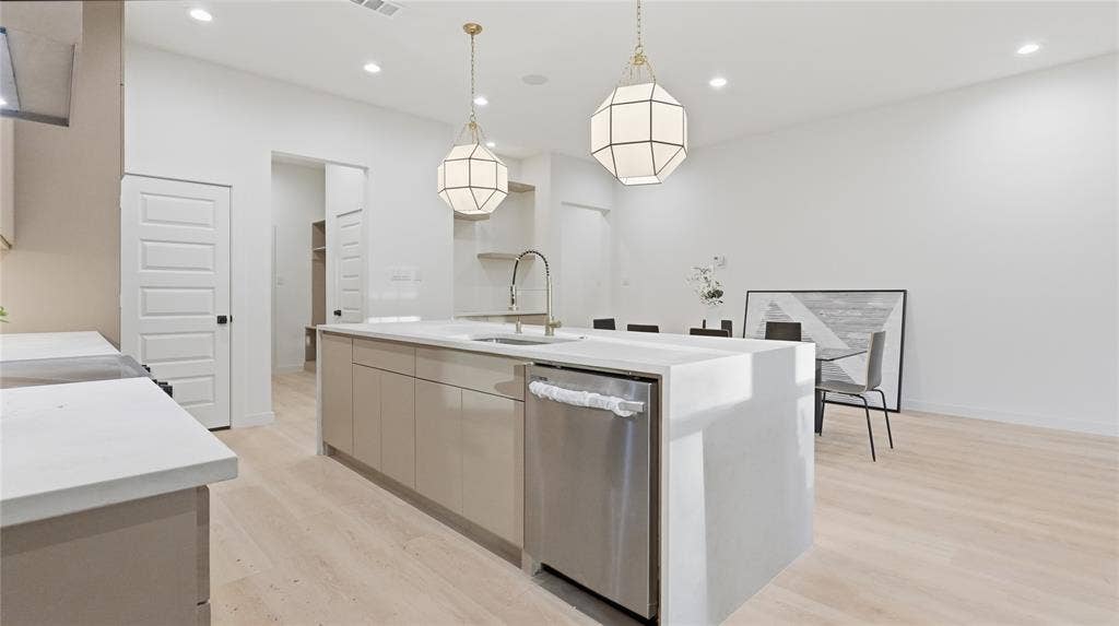 Kitchen featuring a waterfall-edge island with stone-finish countertops, geometric pendant lighting, stainless steel dishwasher, and wood-finish flooring