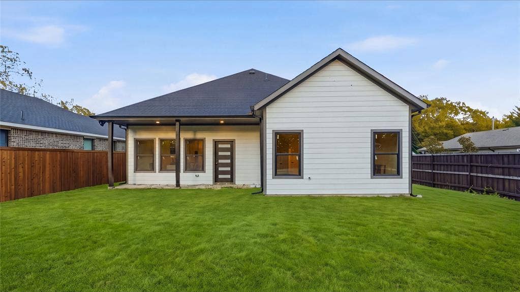 Rear exterior featuring horizontal lap siding, a covered patio with recessed lighting, dark-trimmed windows, a multi-pane glass entry door, and a fenced backyard