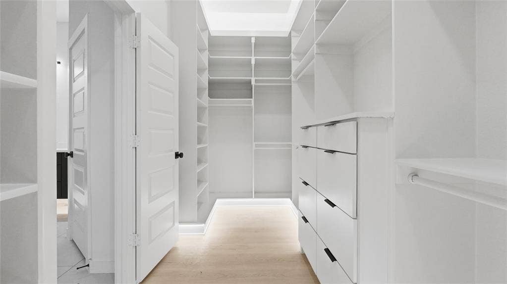 Custom walk-in closet featuring extensive built-in white shelving, integrated hanging rods, a tiered drawer system with matte black hardware, and light-toned wood-finish flooring