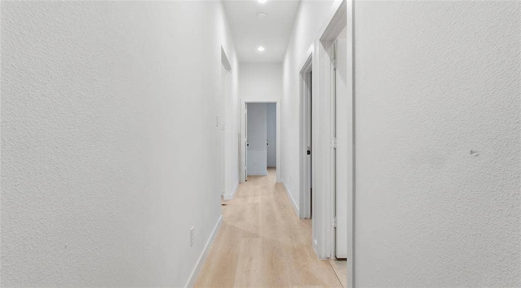 Hallway featuring light-toned wood-finish flooring, crisp white walls, and recessed ceiling lighting