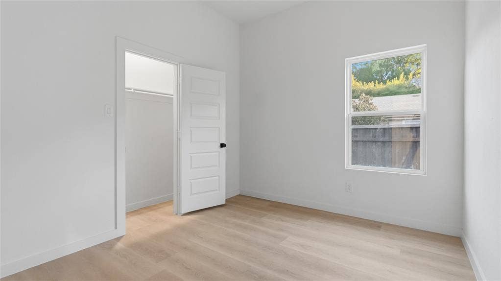 Interior room featuring wood-finish flooring, a five-panel interior door, a walk-in closet, and a single-pane window