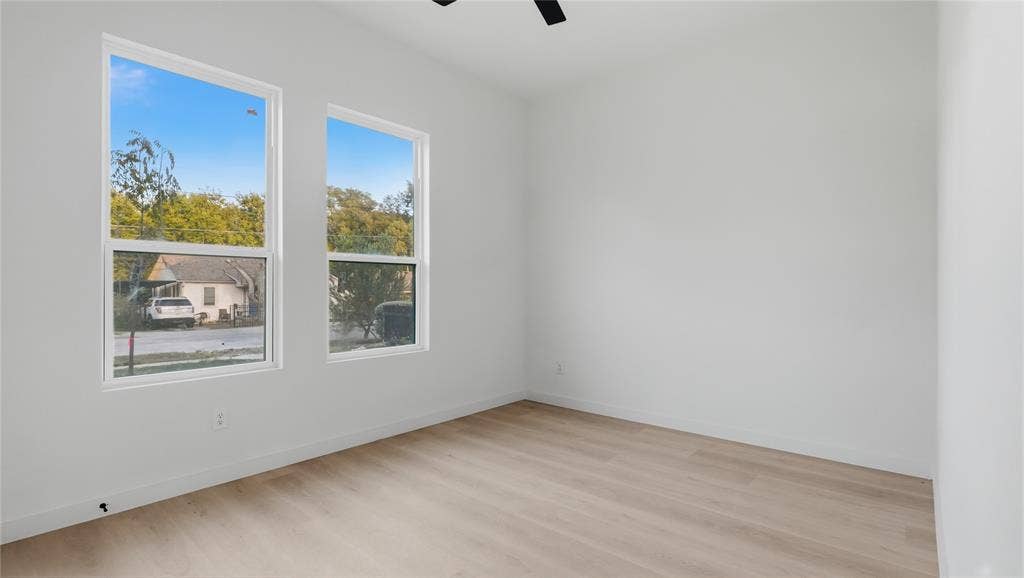 Neutral interior room featuring wood-finish flooring, dual windows with white frames, and a ceiling-mounted fan