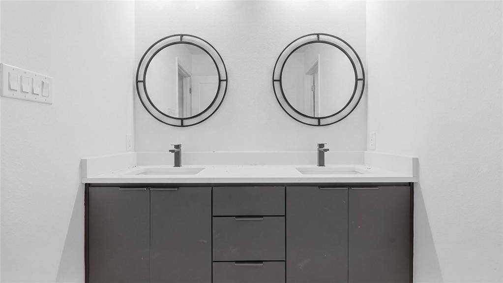 Dual-sink vanity featuring a solid surface countertop, charcoal-toned cabinetry, and two circular mirrors with black frames
