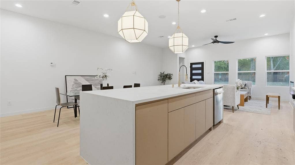 Kitchen featuring a waterfall-edge island with light-toned cabinetry, wood-finish flooring, geometric pendant lighting, and recessed ceiling lights