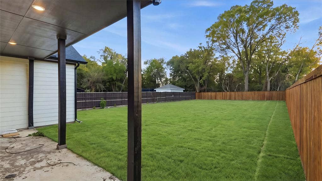 Covered concrete patio with recessed lighting, expansive grass lawn, and full-perimeter wood privacy fencing
