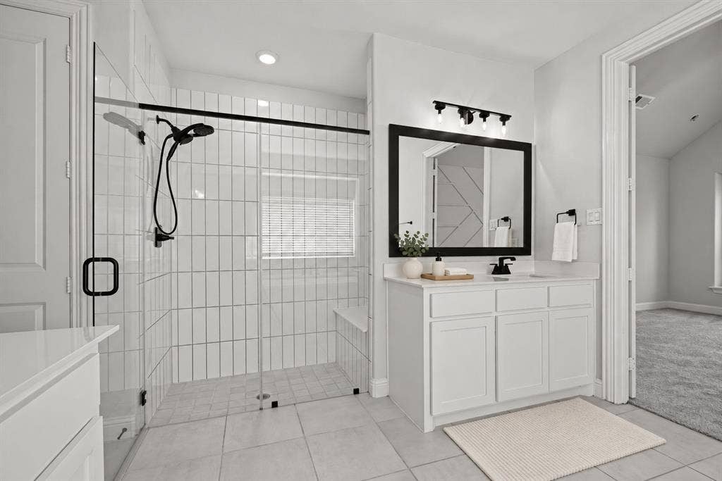 Walk-in shower with vertical tile surround, glass enclosure, and matte black fixtures, paired with a white vanity featuring a solid surface countertop and framed mirror
