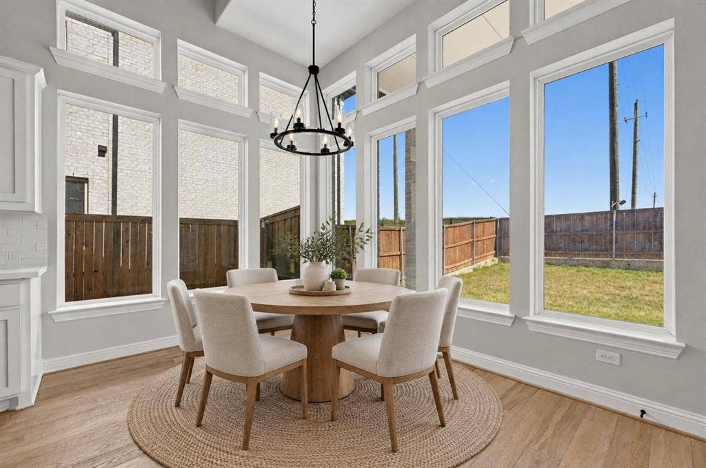 Sun-filled breakfast area featuring expansive floor-to-ceiling windows, clerestory windows, wood-finish flooring, and a modern tiered chandelier