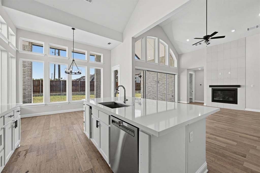 Open-concept interior featuring vaulted ceilings, a central kitchen island with stone countertops, floor-to-ceiling windows, wood-finish flooring, and a fireplace with a floor-to-ceiling tile surround