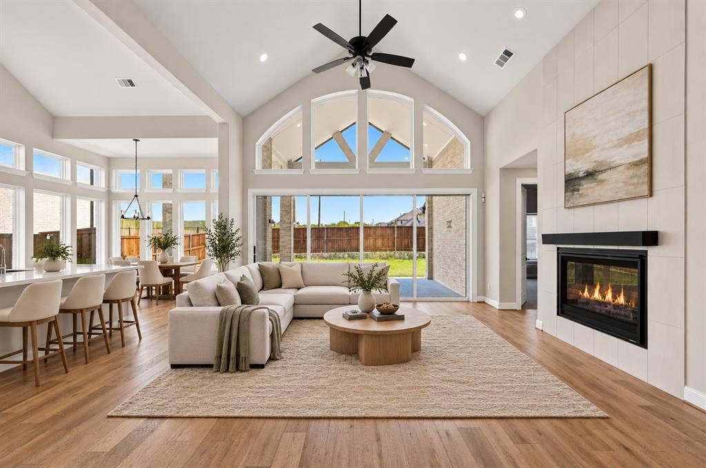 Vaulted ceiling featuring an exposed beam, floor-to-ceiling fireplace with large-format tile surround, expansive multi-pane window wall, and wood-finish flooring
