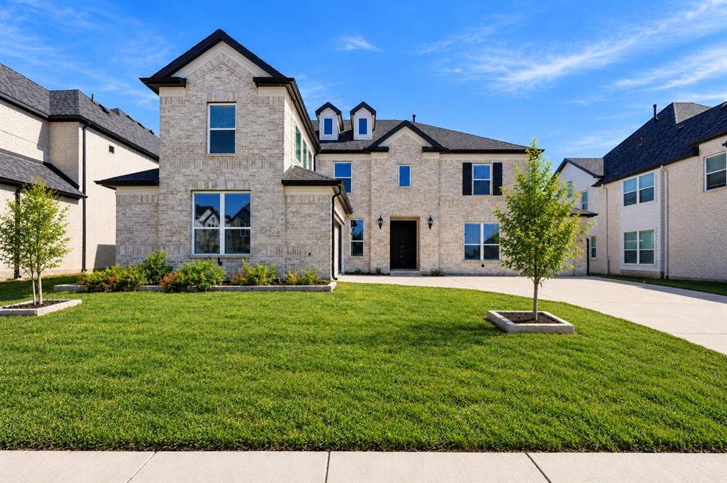 Two-story brick exterior featuring a multi-gabled roofline, dormer windows, shutters, and a concrete driveway