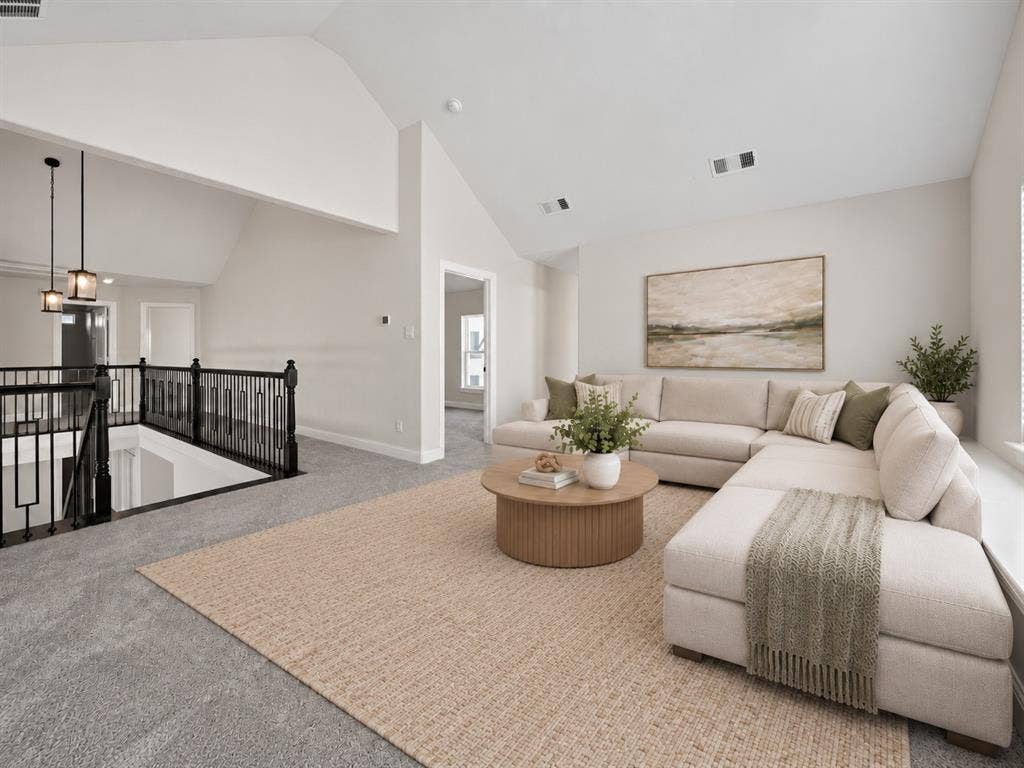 Vaulted ceilings, dark metal railing with vertical balusters, and dual hanging pendant lights
