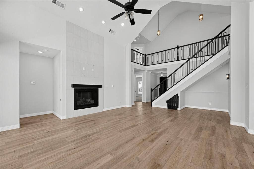 Vaulted ceiling featuring recessed lighting and a central ceiling fan, fireplace with floor-to-ceiling tile surround, and staircase with black metal decorative railing