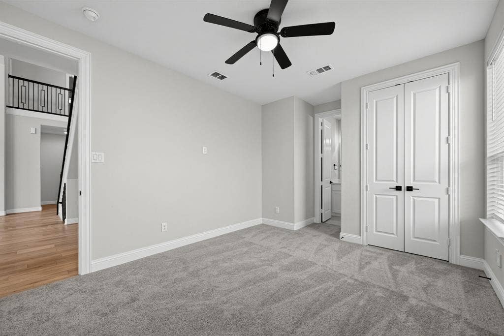 Neutral-toned room featuring plush carpeting, a ceiling fan with integrated lighting, and double doors with matte black hardware