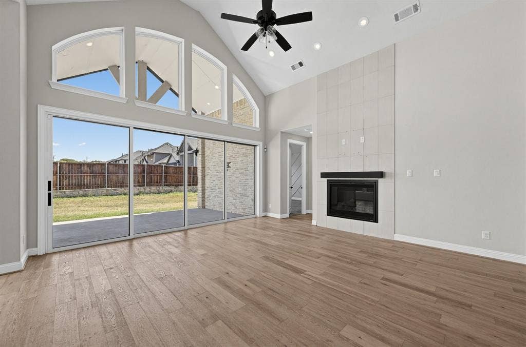 Vaulted ceiling featuring a central black ceiling fan, wood-finish flooring, floor-to-ceiling multi-panel sliding glass doors, and a tiled fireplace surround