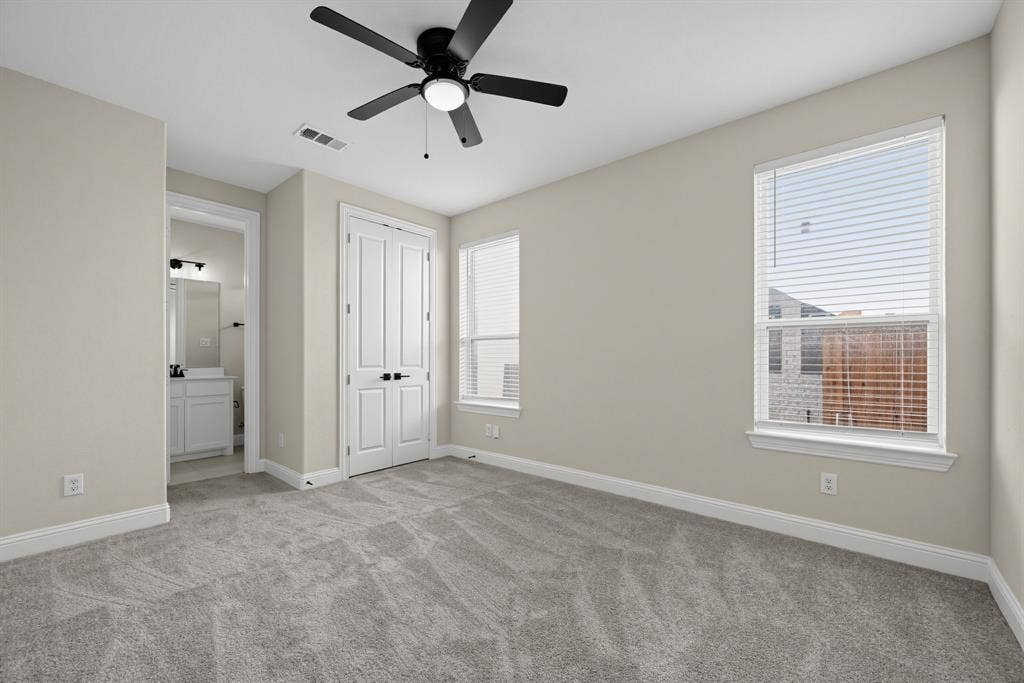 Neutral-toned interior featuring wall-to-wall carpeting, dual windows with integrated blinds, a ceiling fan with integrated lighting, and a double-door closet