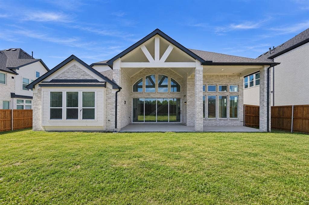 Rear exterior featuring stone veneer siding, an expansive covered patio, arched transom windows, and an open-gable roofline