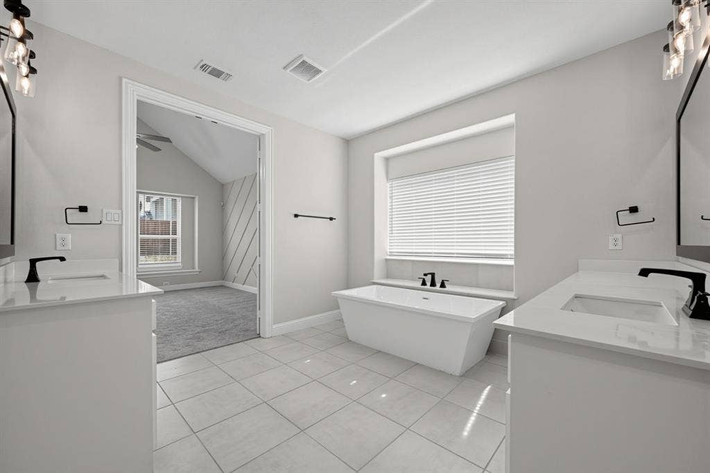 Bathroom featuring dual white vanities with rectangular undermount sinks and light-toned countertops, a freestanding soaking tub, matte black fixtures, and large-format tile flooring