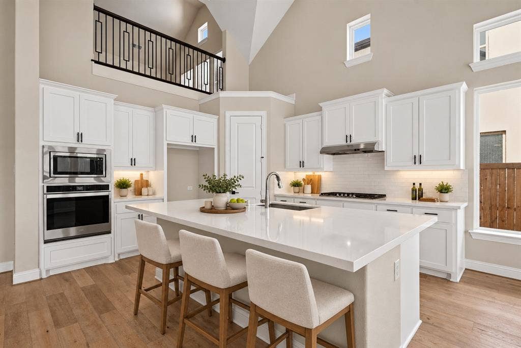 Kitchen featuring white cabinetry, an expansive central island with a solid surface countertop, stainless steel built-in double ovens, vaulted ceilings, and wood-finish flooring