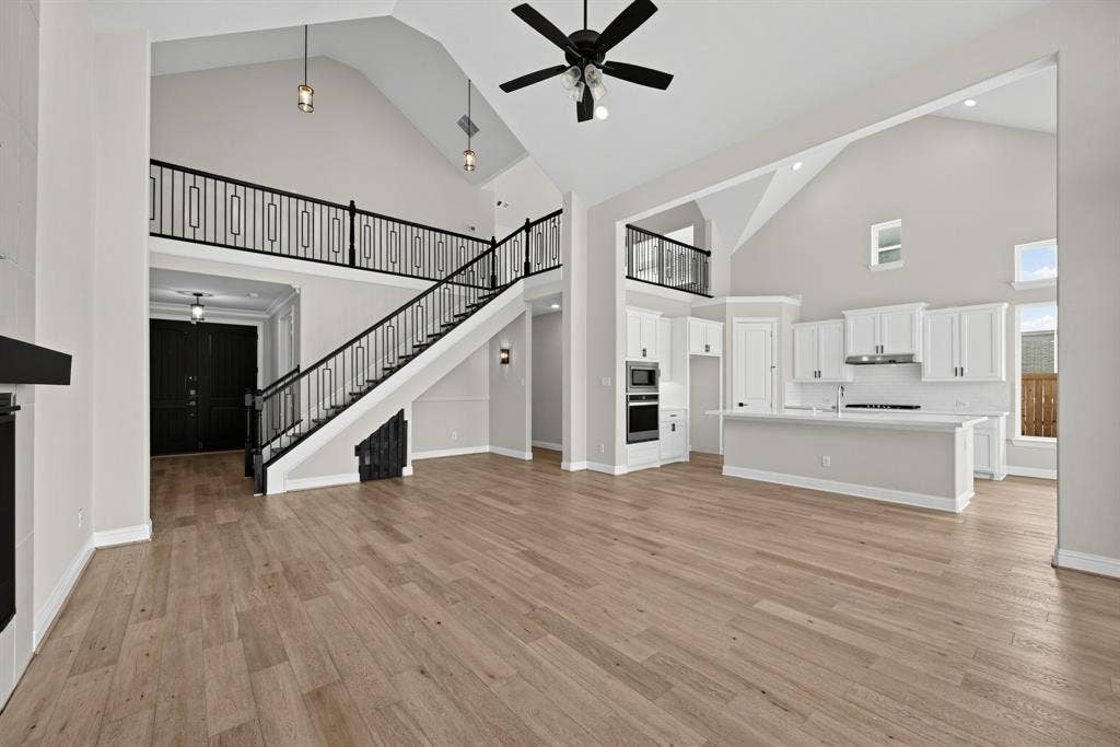 Vaulted ceilings, wood-finish flooring, white cabinetry, a center kitchen island, and a staircase with a black metal railing