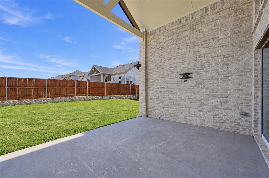 Covered patio featuring a concrete floor, gabled ceiling, brick exterior wall, fenced yard, and stone retaining wall